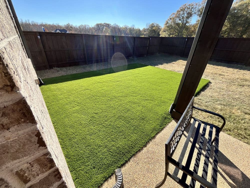 Artificial turf lawn installation in a backyard with a patio and bench.